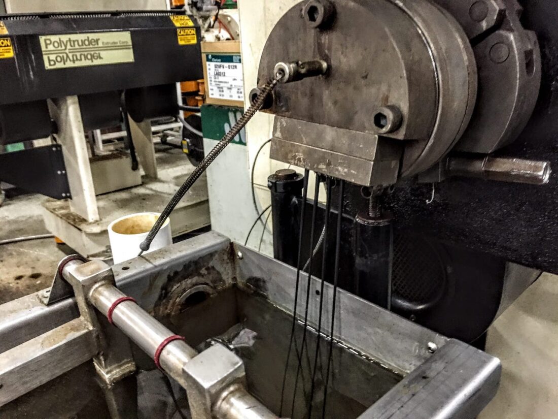 Fresh 3D printer filament emerging from the extruder and entering the cooling water trough.