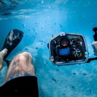 man bathing under the sea while holding black camera