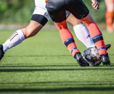 How to Win Money Betting on Soccer? woman in black and white soccer jersey kicking soccer ball on green field during daytime