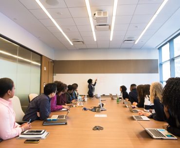 people on conference table looking at talking woman