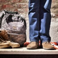 minimalist photography of person standing near backpack and boots