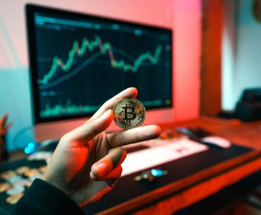 What Features of Bitcoin Are So Tempting? a person holding a coin in front of a computer