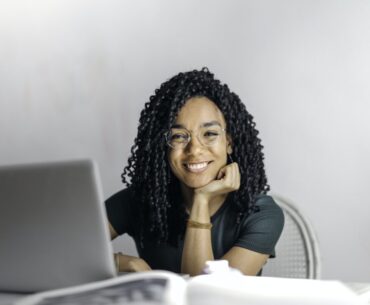 Happy ethnic woman sitting at table with laptop