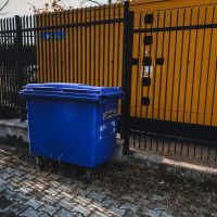 blue trash bin beside yellow metal fence