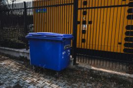 Where to Get Reliable 30 Yard Dumpster Rental Near Me in Las Vegas blue trash bin beside yellow metal fence