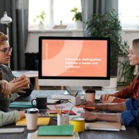 A multicultural team collaborating in an office, discussing a project with a visible monitor.