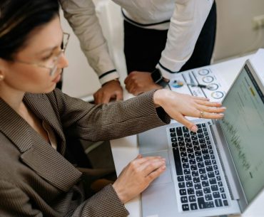 Low Overhead, High Potential: Why Insurance Agencies Make Sense Two professionals focused on analyzing data charts on a laptop in an office setting.