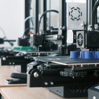 A row of 3D printers creating blue plastic cylinders on a wooden workbench