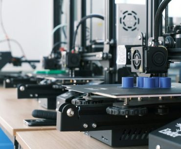 Can a 3D Printing Side Hustle Actually Fund Your Retirement? A row of 3D printers creating blue plastic cylinders on a wooden workbench