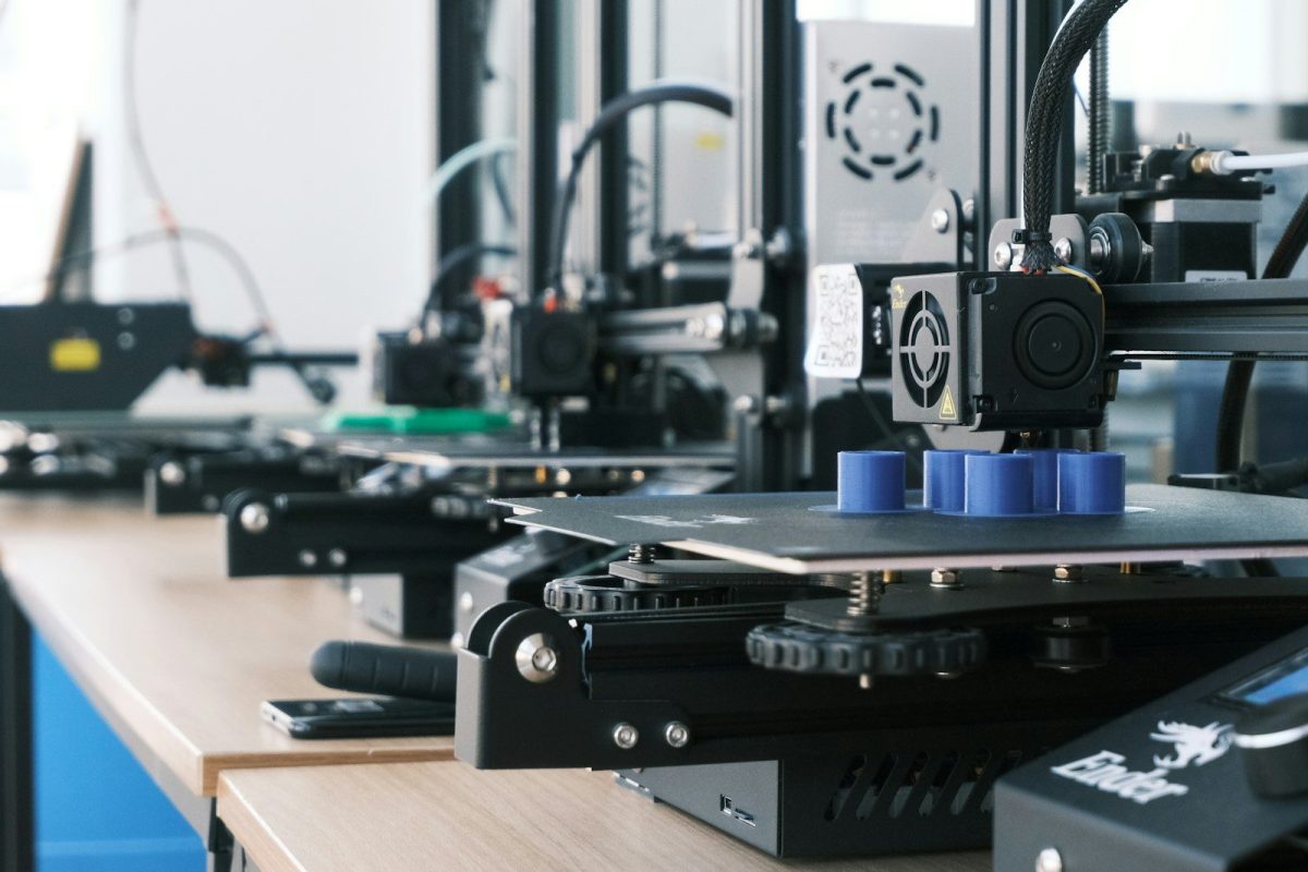 Can a 3D Printing Side Hustle Actually Fund Your Retirement? A row of 3D printers creating blue plastic cylinders on a wooden workbench