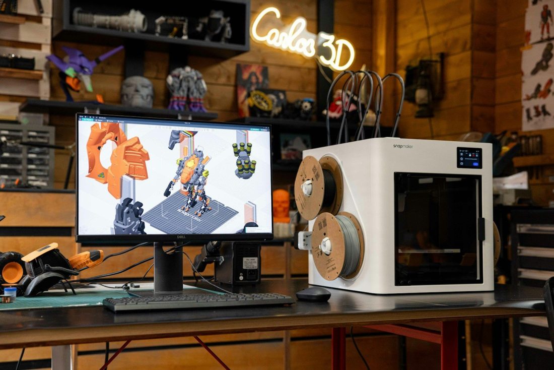 3D printer with computer displaying design on desk