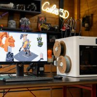 3D printer with computer displaying design on desk