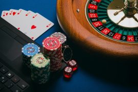 A roulette wheel, poker chips, playing cards, and dice on a laptop keyboard